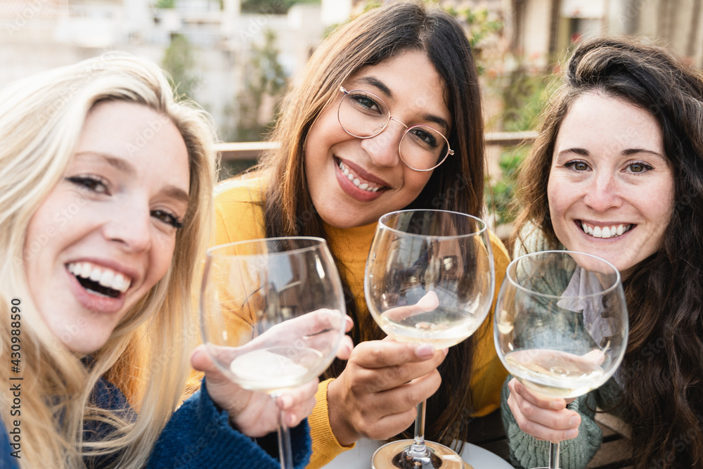 Multiracial friends doing selfie with mobile phone while cheering with wine outdoors in patio restaurant - Focus on african girl Multiracial friends doing selfie with mobile phone while cheering with wine outdoors in patio restaurant - Focus on african girl