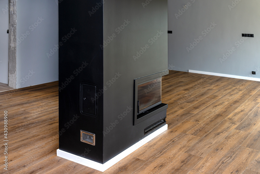 A modern fireplace with a closed combustion chamber standing in the living room, painted black, with a corner pane covered with soot. A modern fireplace with a closed combustion chamber standing in the living room, painted black, with a corner pane covered with soot.