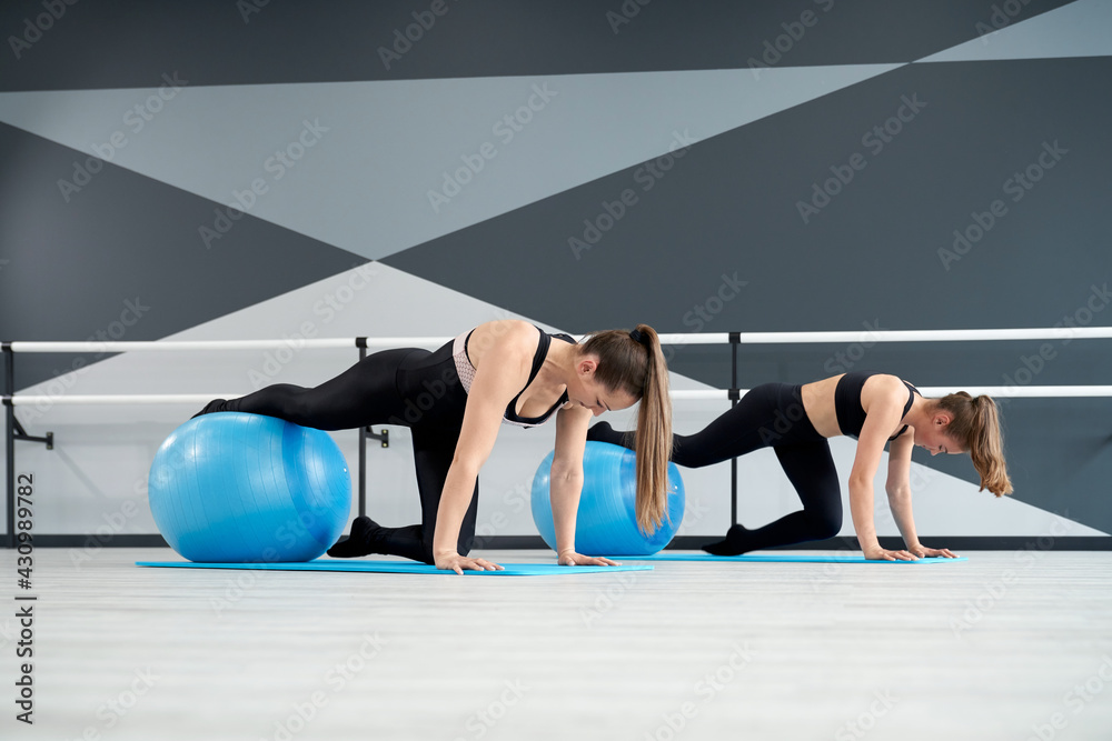 Side view of two attractive fit women training core muscles with one