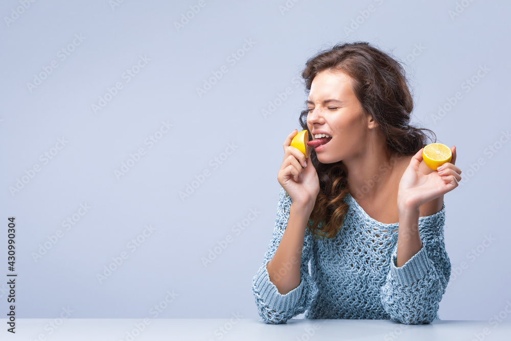 Cute brunette woman holding two halves of yellow lemon citrus fruit in hands and biting wth appetite first half Cute brunette woman holding two halves of yellow lemon citrus fruit in hands and biting wth appetite first half