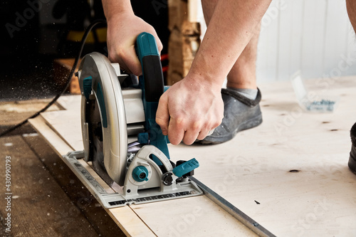 Sawing plywood by circular saw. Home repair. Hand tool. Man hold equipment. Building process. Woodworking. Safety engineering. Without gloves. Copy space. Indoor. Cutting material. Rental instrument