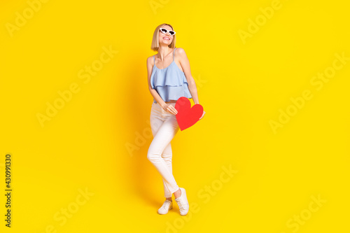 Full body photo of optimistic nice blond hair lady hold heart wear spectacles top pants isolated on yellow background