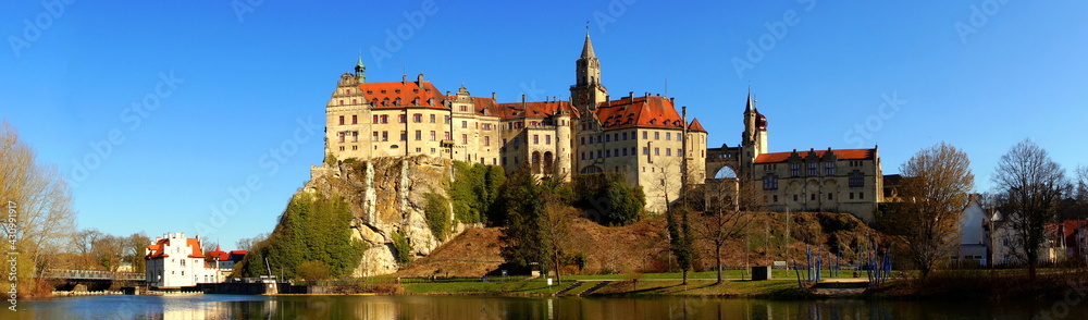 weites Panorama von Schloss Sigmaringen unter blauem Himmel und Ufer der Donau mit Stauwehr