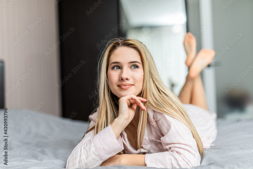Beautiful young woman adjusting her hair and looking at camera while lying on the bed at home Beautiful young woman adjusting her hair and looking at camera while lying on the bed at home