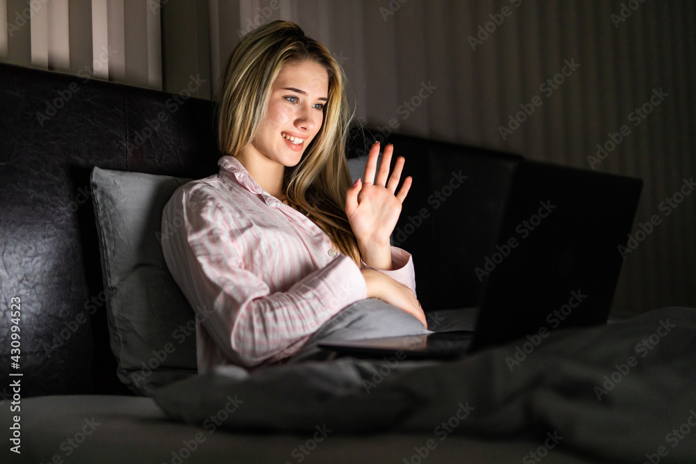 technology, internet, communication and people concept - happy smiling young with laptop computer having video call in bed at home at night technology, internet, communication and people concept - happy smiling young with laptop computer having video call in bed at home at night
