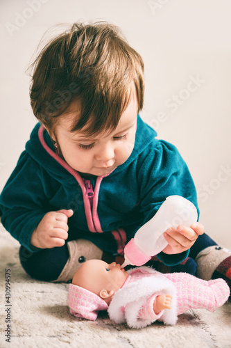 Baby girl playing with a doll, feeding a doll from a bottle, taking care of a doll. Life style and childhood.
