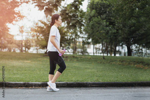 Woman exercise walking in  the park with hand holding bottle water.