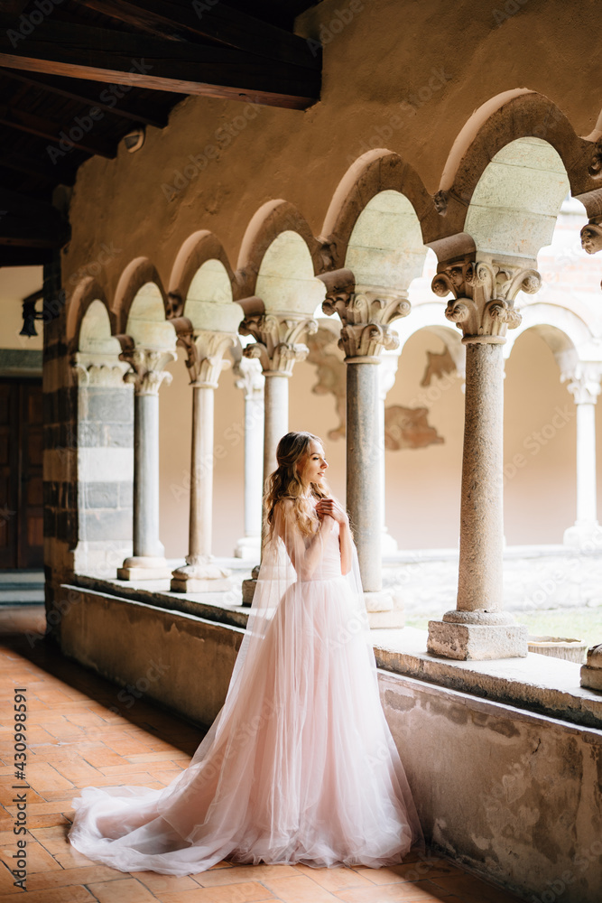 Bride stands with her arms crossed on her chest on a loggia with columns in an old villa on Lake Como