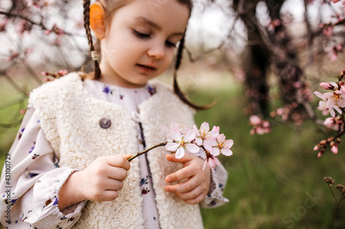 Little girl holding a small branch with pink cherry flowers, in garden, outdoors.