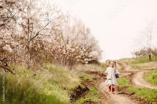 Little girl in rubber boots running on a path in countryside on spring day.