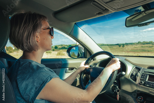 Portrait of serious woman in sunglasses driving car in motion through fields in countryside
