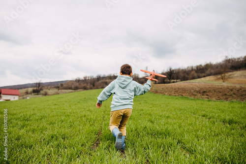 Boy playing with a red plane in a field with green grass, running.