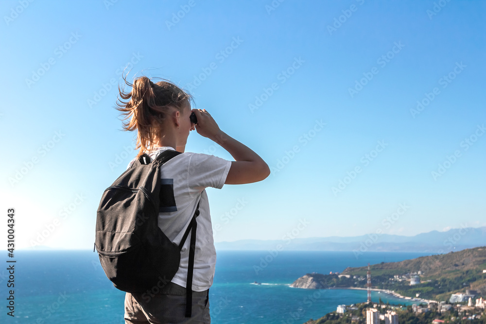 Back view of girl traveler looking through binoculars at panoramic view with sea and blue sky during summer holiday on seaside Back view of girl traveler looking through binoculars at panoramic view with sea and blue sky during summer holiday on seaside