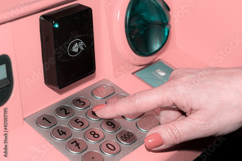 A woman's hand dials the PIN code on the bank's ATM. A young woman enters a PIN code on the ATM keyboard. photo