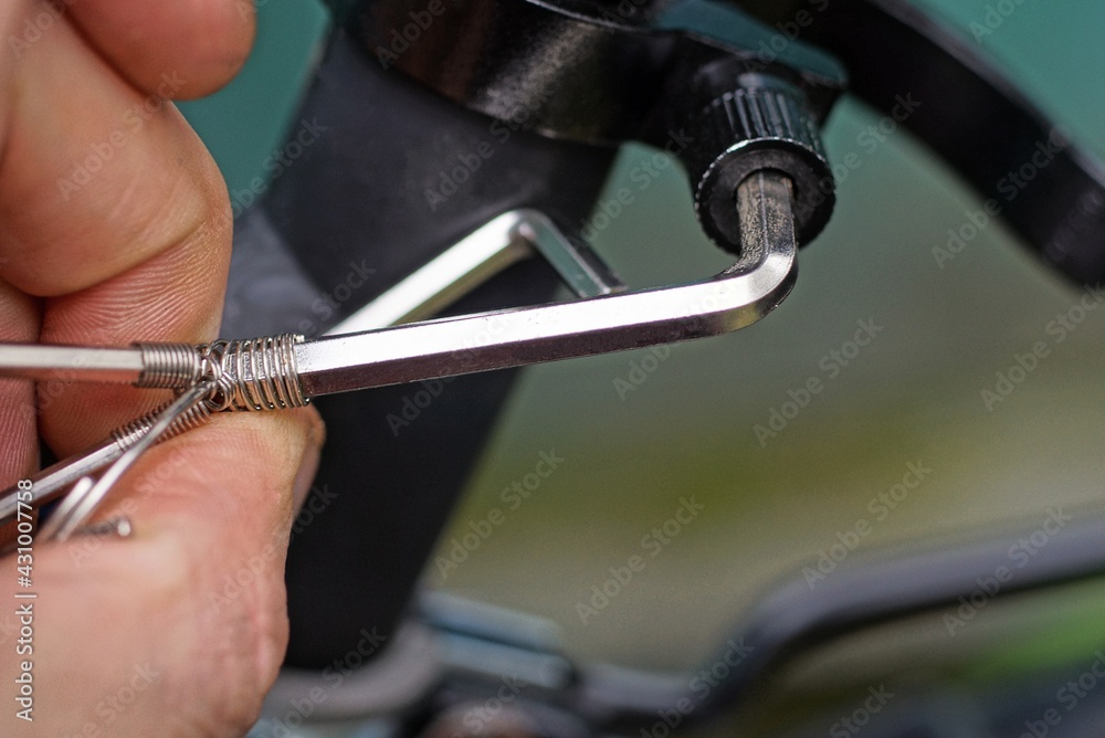 gray metal wrench in hand tightens a black nut on a bicycle