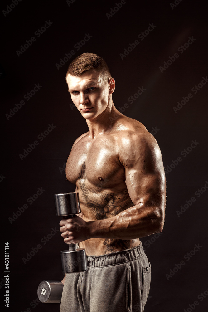 Serious tattoed shirtless athlete lifting metal dumbbells training on dark background