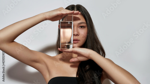 Cute young asian girl hiding face behind glass