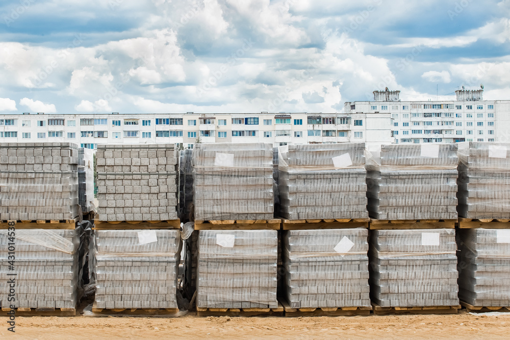 Fototapeta premium A pile of packed paving stone slabs industrial materials at a construction site against the background of old high-rise buildings
