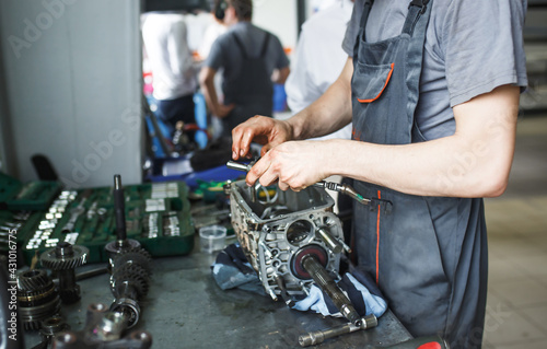 Fototapeta Naklejka Na Ścianę i Meble -  The hand of a car repairman with keys and a special tool on the background of the service area. A mechanic repairs the engine in a car service station in uniform. Copy space
