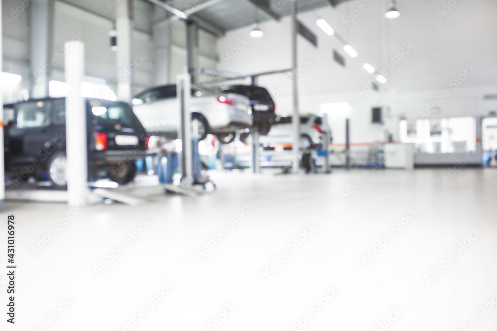 Fototapeta premium Car repair service in defocus, industrial background. Cars on lifts, transport service area, the mechanic repairs the car. Copy space