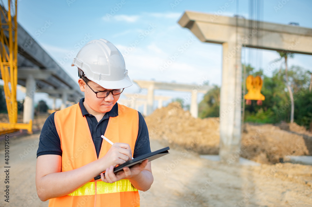 Smart Asian worker man or male civil engineer with protective safety helmet and reflective vest using digital tablet for project planning and checking architectural drawing at construction site. Smart Asian worker man or male civil engineer with protective safety helmet and reflective vest using digital tablet for project planning and checking architectural drawing at construction site.