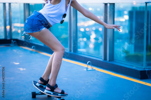 Asian young women surf skate or skates board outdoors on beautiful summer day. Happy young women play surf skate at roof top cityscape.