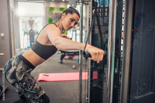 Attractive woman trains arms and triceps on a pulley exercise machine.