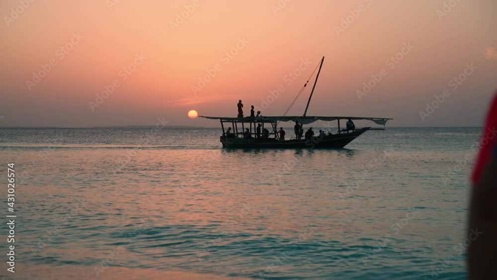 the silhouette of a frigate floats on the horizon along the sea against the background of a colorful sunset, dancing people are visible on it