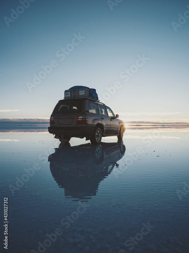 Offroad car SUV jeep of tour group on Salar de Uyuni salt flat lake in Bolivia andes mountains sunrise mirror reflection