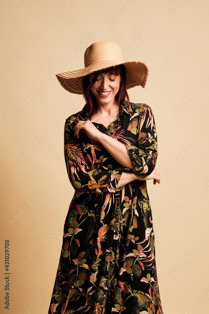 Pretty redhead woman smiling with a long floral dress and hat. Full-length, with boots and a yellow background. Pretty redhead woman smiling with a long floral dress and hat. Full-length, with boots and a yellow background.