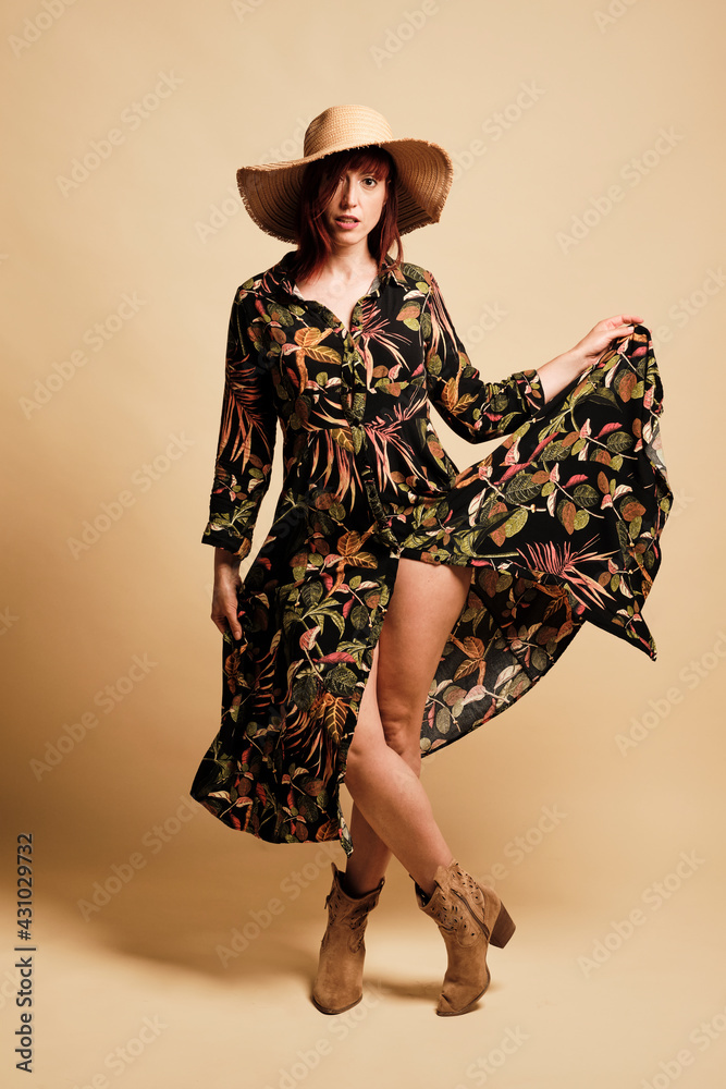 Pretty redhead woman smiling with a long floral dress and hat. Full-length, with boots and a yellow background. Pretty redhead woman smiling with a long floral dress and hat. Full-length, with boots and a yellow background.
