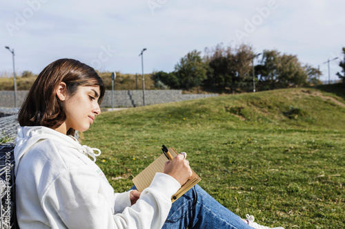 Young beautiful woman writing in notebook outdoors in public park, taking notes - Millennial people and education concept