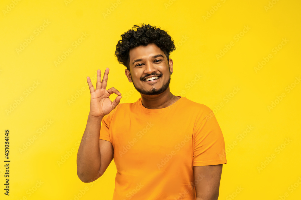Cheerful smiling Indian man showing gesture okay hand and looking at camera, yellow background with place for text. Proposition of work Cheerful smiling Indian man showing gesture okay hand and looking at camera, yellow background with place for text. Proposition of work