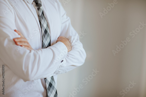 Man in white shirt and grey squared tie posing hands crossed in the white room. Copy space. Focus is at the hands.Business concept.