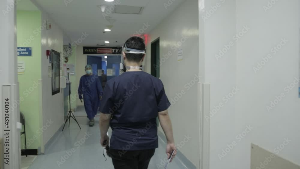Back View Handheld Following Shot of Young Male Doctor Well-Equipped Passing Hospital Bed in Corridor and Entering Emergency Room, 4K Back View Handheld Following Shot of Young Male Doctor Well-Equipped Passing Hospital Bed in Corridor and Entering Emergency Room, 4K