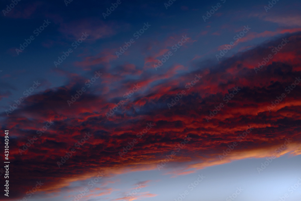 Nahaufnahme einer abstrakten, rot gefärbten Wolke am blauen Abendhimmel