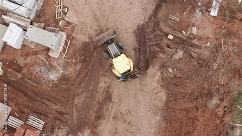 The yellow tractor drives on the site next to the building under construction. Brick and concrete blocks, a blurred road. Builders in protective helmets. High quality. 4k footage.