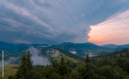 Amazing rainy sunset clouds over Carpathian green mountains. Beautiful summer dusk scenery after the rain.