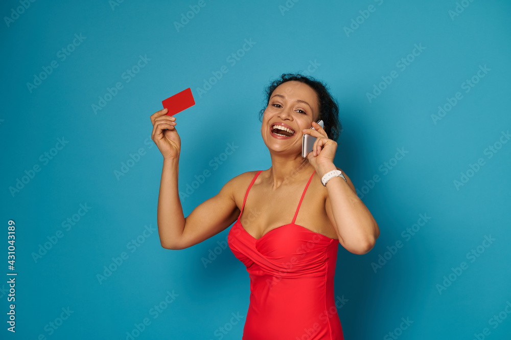 Cute brunette with beautiful smile talking on smartphone and holding a red blank card while smiling to the camera Cute brunette with beautiful smile talking on smartphone and holding a red blank card while smiling to the camera
