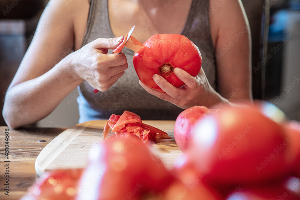 Ταπετσαρία woman is peeling a lot of red fresh and boiled tomatos with a knife, preparing f