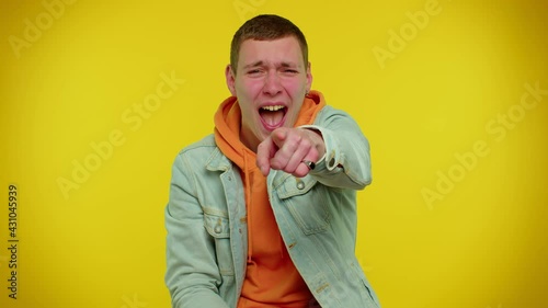 Teen stylish boy showing loser gesture and pointing on you, blaming accusing for unsuccess, expressing disrespect, mocking your failure, bullying abuse. Young man on yellow studio background
