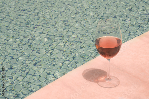Crystal goblet with rose wine on the edge of a swimming pool. High class people drink concept.