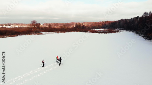 Aerial of winter snowshoeing across valley on sunset. Breathtaking natural landscape. Active group people in winter clothes snowshoeing on snowy lake. Travelers snowshoe explore locality
