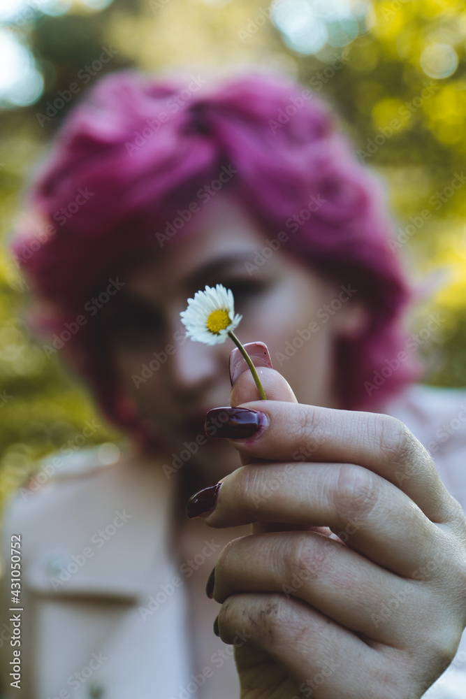 Mujer sujetando una flor en la mano, Margarita enfocada en primer plano, Mano sujetando una margarita y el fondo desenfocado , mujer de pelo rosa sujetando una flor
