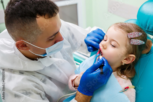 A professional doctor  a children s dentist  treats a little girl s teeth with instruments. Dental office for patient examination. The process of dental treatment in a child