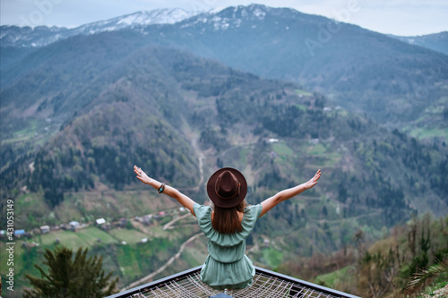 Free boho chic woman traveler sitting with open arms and enjoying of mountain landscape. Calm and quiet wanderlust concept moment when person feels happiness and freedom
