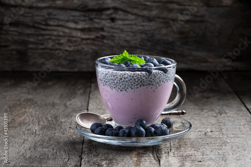 Purple blueberry yogurt with fresh berries chia seeds in glass cup on wooden table