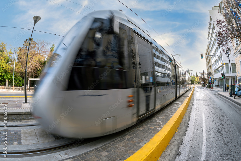 Naklejka premium The Athens city tram train is approaching the central station at Syntagma square. Tram in motion. Sunny day with cloudy blue sky in Athens, Greece.