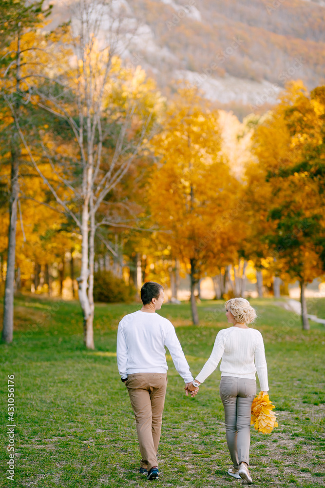 Man and woman in white sweaters and beige trousers are hugging each other while go into the forest. Back view. Close up