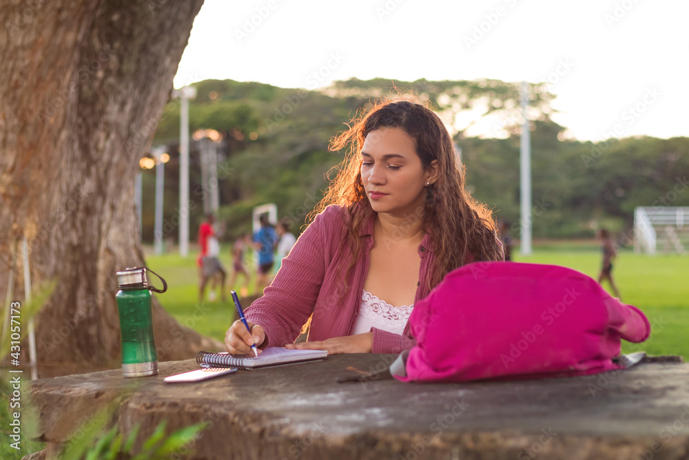 Enfoque selectivo de una mujer universitaria colombiana escribiendo encima de una mesa de madera debajo de un árbol